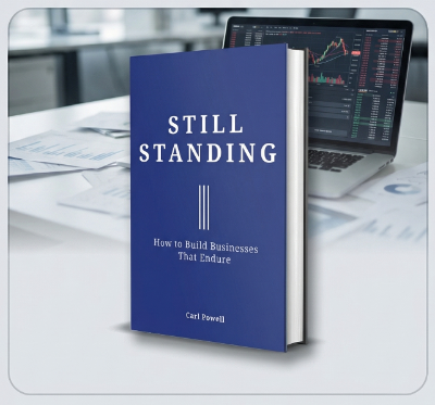 Book titled 'Still Standing' by Carl Powell on a desk with a laptop and financial documents.